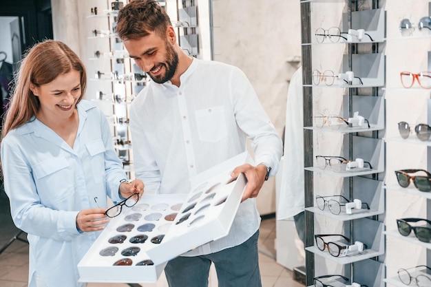 De pie y sonriendo Hombre y mujer en la tienda de gafas Ayudando a elegir el producto