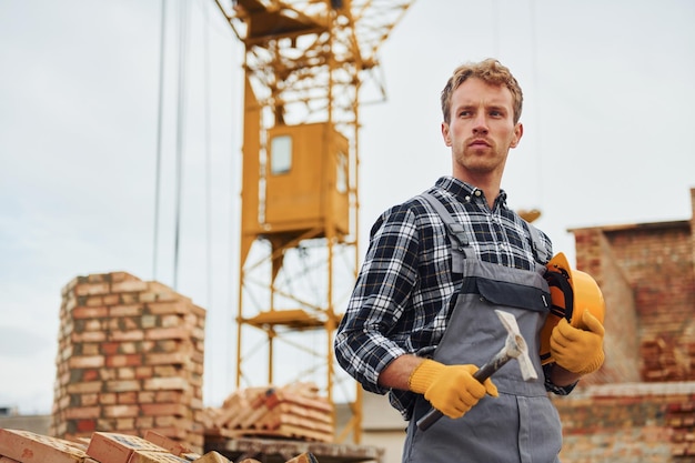 De pie y sostiene casco con martillo Trabajador de la construcción en uniforme y equipo de seguridad tiene trabajo en la construcción