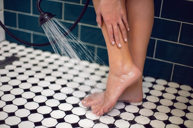 El pie de Woma en la cabina de la ducha se lava con una ducha bajo un chorro de agua sobre un azulejo blanco y negro