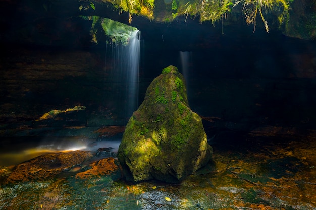 Piedra cubierta de musgo con cueva en el fondo con cascada