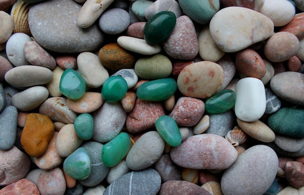 Piedras de aventurina lisas en bruto sobre guijarros redondos mezclados con pequeñas conchas marinas