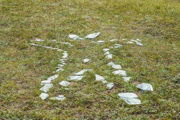 Piedras blancas dispuestas sobre la hierba verde en forma de hombre. Fondo de naturaleza de arte con piedras en el suelo en forma de carácter. Cementerio pagano de Altai. Antiguo lugar de enterramiento pagano de los altaianos. Rito pagano en Altai