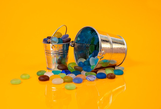 Piedras de colores en vidrio en tarro en balde sobre fondo naranja