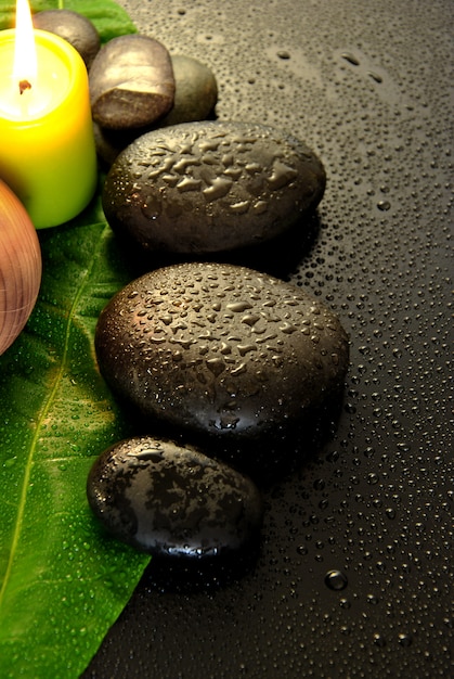 Piedras de masaje mojado con hojas verdes y gotas de agua.