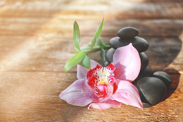 Piedras de spa con bambú y orquídea rosa sobre fondo de madera