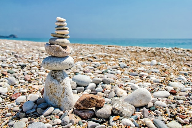 Piedras zen apiladas en la playa contra un cielo azul y un océano con espacio de copia