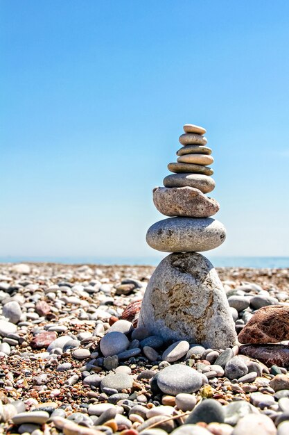 Piedras zen apiladas en la playa contra un cielo azul y un océano con espacio de copia