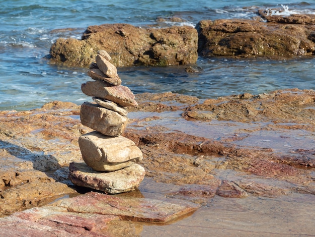 Piedras zen equilibradas en la playa con cielo azul y mar.