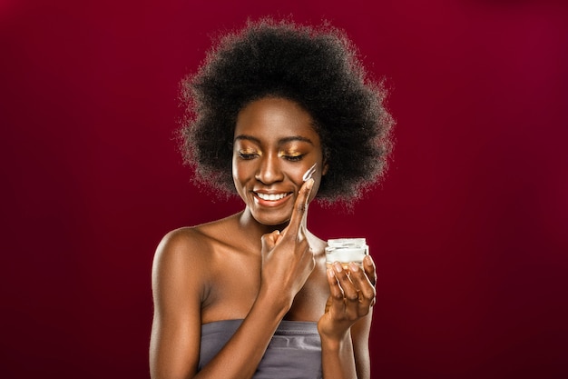 Piel perfecta. Encantado de agradable mujer sonriendo mientras se pone crema en la mejilla