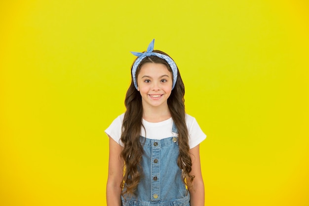 Piensa positivo. chica retro sonriendo fondo amarillo. aspecto vintage de niño pequeño. moda infantil de verano. belleza y moda. infancia feliz. concepto de salón de peluquería. pequeña belleza pelo largo y rizado.