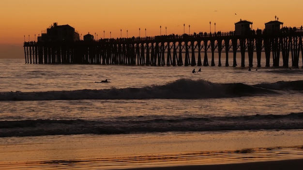 Pier silueta al atardecer, California, Estados Unidos, Oceanside. Resort de surf, playa tropical oceánica. Surfista esperando ola.