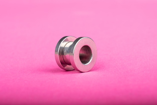 Foto piercing del túnel de la oreja de plata sobre fondo rosa closeup