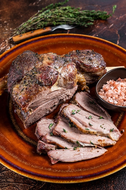 Pierna de cordero de cordero asado a la barbacoa en rodajas en un plato rústico. Fondo oscuro. Vista superior.