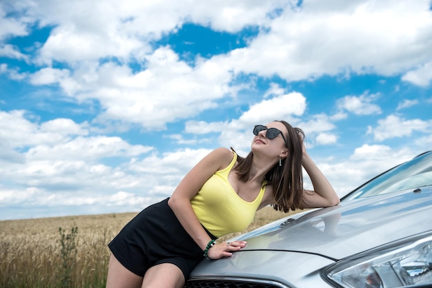 Pierna hermosa cerca del coche posando en la orilla arenosa durante las vacaciones de verano