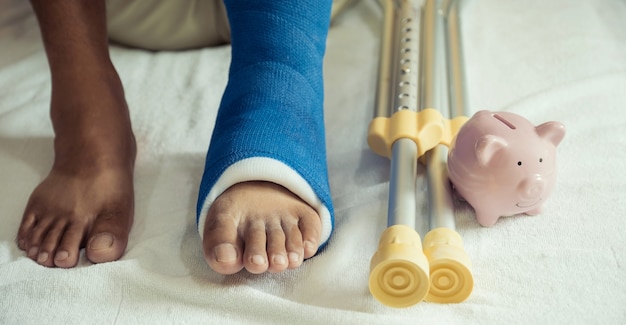 La pierna del hombre usa muletas para caminar después de la cirugía recuperación lesión huesos rotos con hucha rosa.