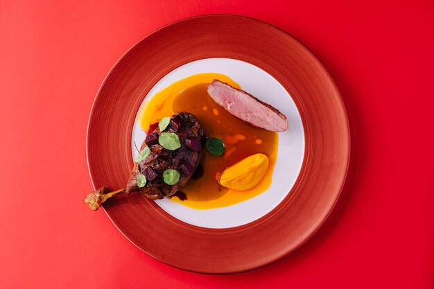 Foto pierna de pato con puré de calabaza en un plato rojo