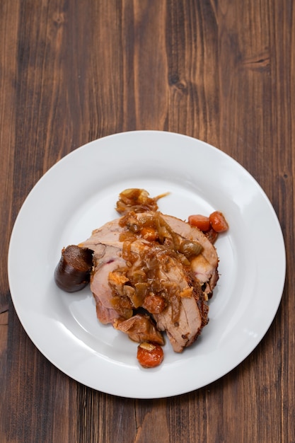 Pierna de pavo al horno con verduras, salchicha ahumada y hierbas en un plato blanco