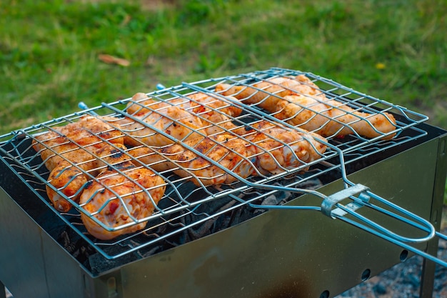 Las piernas y las alas de pollo se fríen a las brasas en un brasero en una parrilla de barbacoa. El pollo marinado se fríe en un picnic.