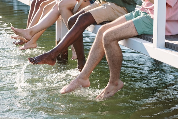 Piernas de amigos descalzos salpicaduras de agua en el lago