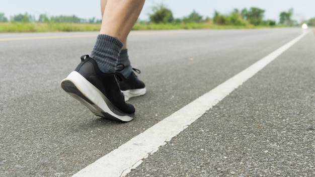 Foto las piernas de los atletas masculinos con zapatos negros se están preparando para correr en el camino pavimentado ejercicio al aire libre para perder peso y buena salud. fitness y estilo de vida saludable competencia y concepto exitoso.