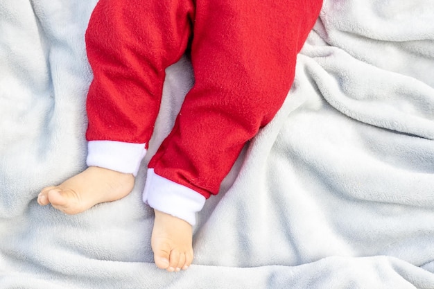 piernas de bebé en pantalones de color rojo de santa claus de navidad.concepto de vacaciones de navidad.niño pequeño acostado en gris