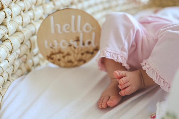 Foto piernas de un bebé recién nacido y una tabla de madera con la inscripción hola mundo