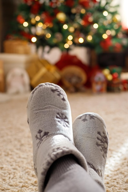 Piernas en un cálido hogar zapatos disfrutando de las vacaciones de invierno en el fondo del árbol de Navidad luces bokeh Navidad vacaciones de Año Nuevo