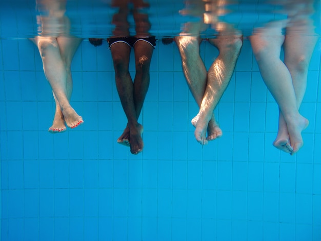 Piernas de cuatro personas bajo el agua en la piscina