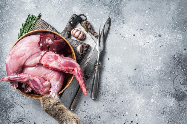 Piernas y despojos de carne de caza de liebre cruda en plato de madera con hierba Fondo gris Vista superior Espacio de copia