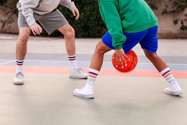 Piernas de dos amigos irreconocibles jugando baloncesto en un tribunal de la ciudad concepto de deporte urbano en la calle