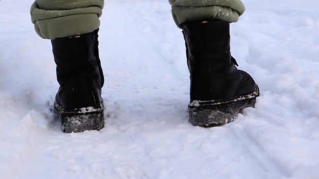Piernas femeninas con botas negras, caminar en la nieve en invierno. Mujer activa alejándose de la cámara en el bosque de invierno. Concéntrate en tus piernas. Hermoso clima de invierno blanco con nevadas frescas.