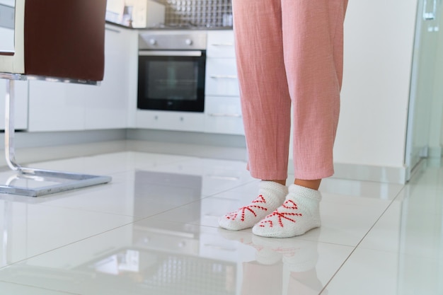 Piernas femeninas con cómodos y cómodos calcetines de punto suave en el suelo cálido y calentado en la cocina de casa