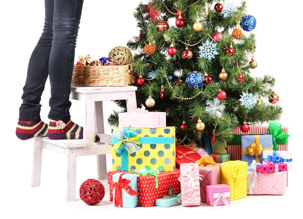 Piernas femeninas en escalera de madera cerca del árbol de Navidad y regalos aislados en blanco