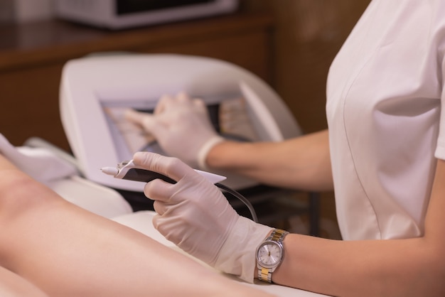 Piernas femeninas en hoja morada durante la depilación por una esteticista profesional con guantes. Spa, industria de la belleza, tratamiento en clínica, electrólisis.