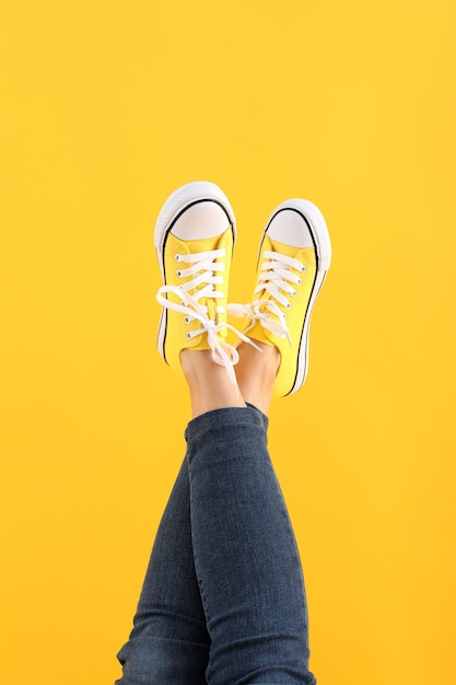 Piernas femeninas en jeans y zapatillas sobre fondo amarillo
