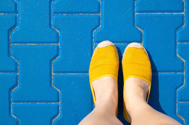 Piernas femeninas en zapatos amarillos sobre un azulejo azul