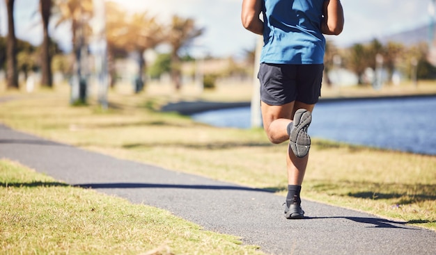 Piernas de fitness y hombre o corredor al aire libre para hacer ejercicio o correr en un parque Primer plano y pies de un atleta masculino en la naturaleza para una carrera de entrenamiento y rendimiento cardiovascular para la salud y el bienestar