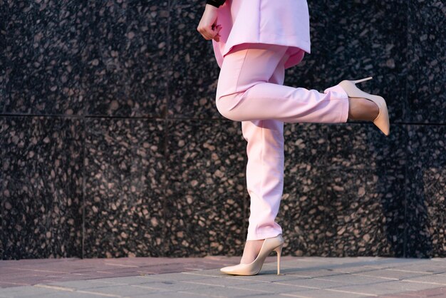 Piernas gráciles de una mujer de negocios con pantalones rosas y zapatos beige