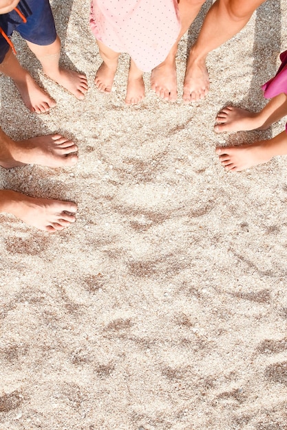 A las piernas de la hermosa familia entera en la arena cerca del fondo del mar