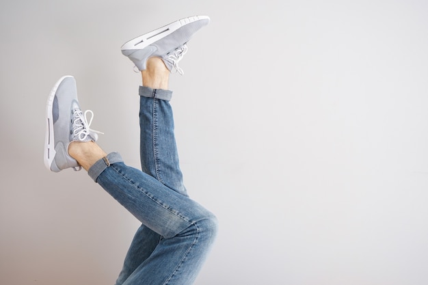 Foto piernas de un hombre joven en jeans y zapatillas sobre un fondo gris.