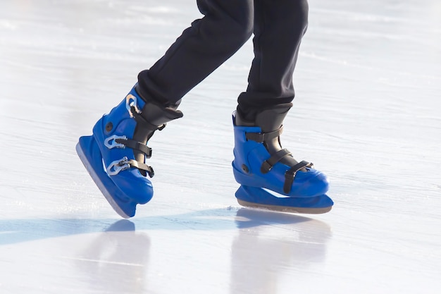 Las piernas de un hombre en patines azules cabalga sobre una pista de hielo