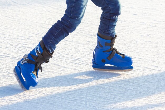 Las piernas de un hombre en patines azules cabalga sobre una pista de hielo