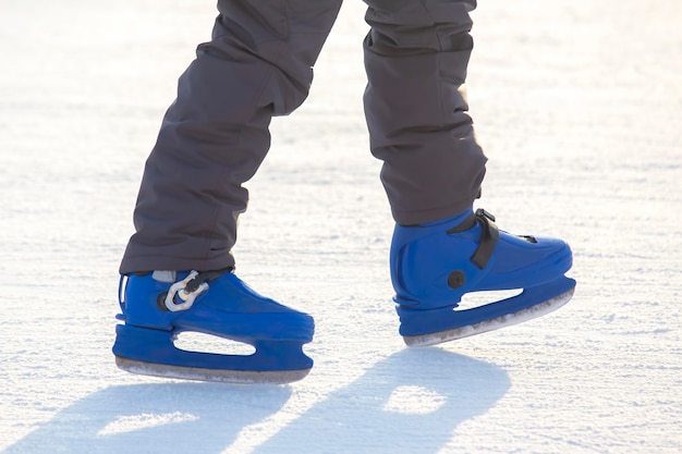 Las piernas de un hombre en patines azules cabalga sobre una pista de hielo