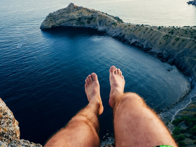 piernas de un hombre sentado en una montaña sobre el mar en el camping turístico