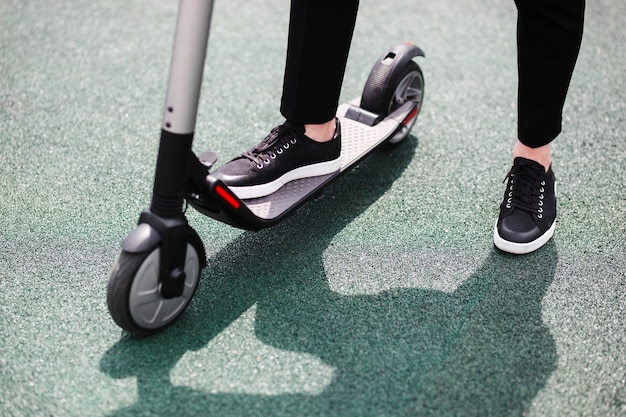 Las piernas de un hombre con traje elegante se colocan en scooter eléctrico en la calle.