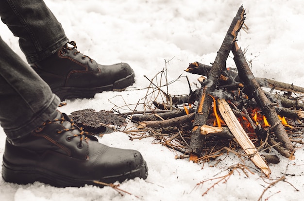 Piernas de hombres con botas de montaña negras cerca de una hoguera ardiente.