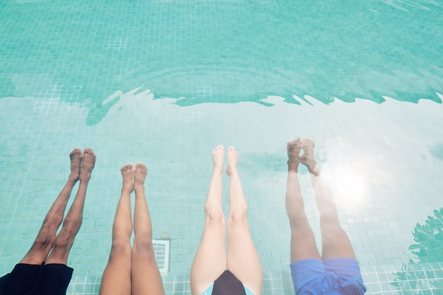 Piernas de hombres y mujeres jóvenes relajándose en la piscina en un caluroso día de verano