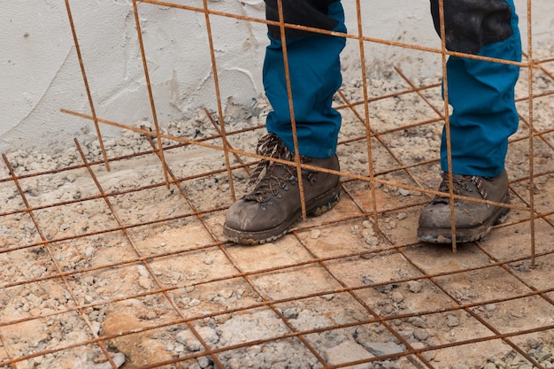 Piernas de hombres trabajando en la construcción con malla de alambre oxidada en el suelo