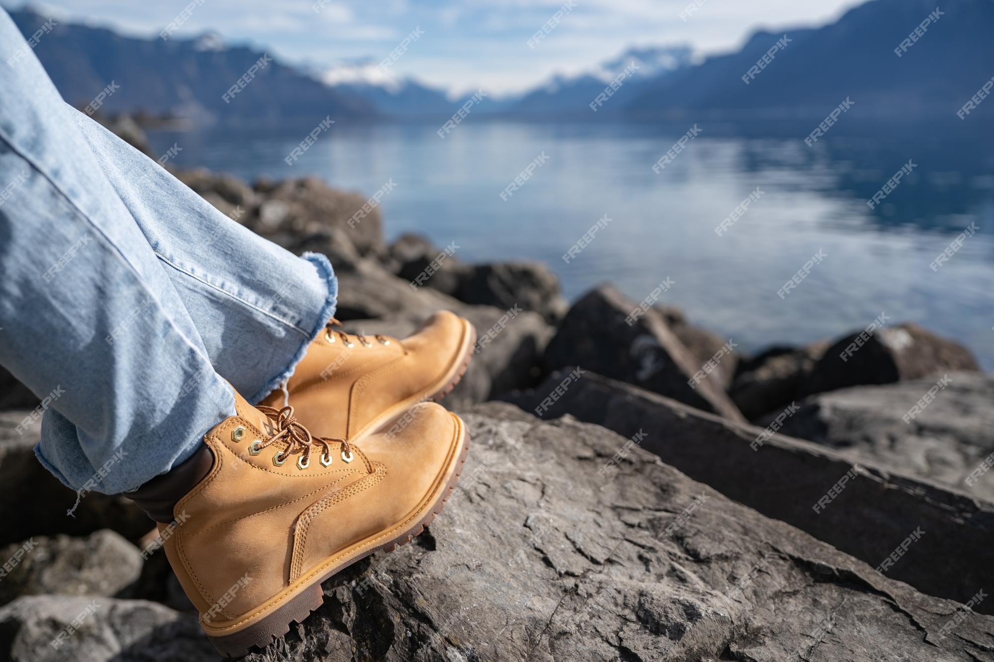 Piernas en jeans y botas de montaña en rocas cerca del lago de montaña con reflejo de agua | Foto Premium