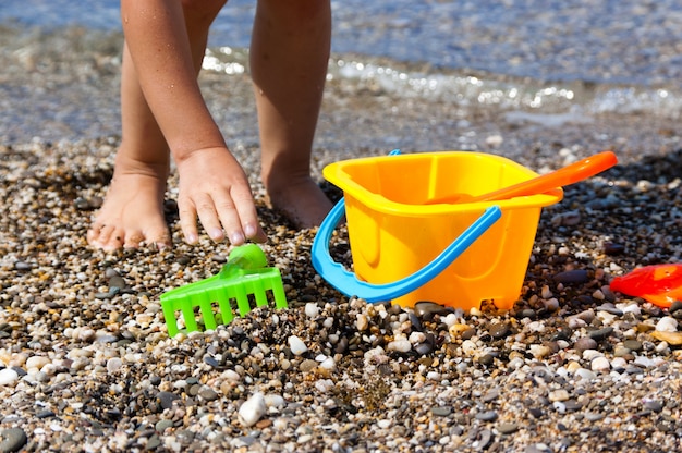 Las piernas y los juguetes del niño en la playa.